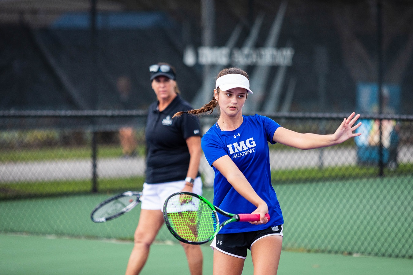 Female tennis player hits a shot while a coach looks on | IMGAcademy.com