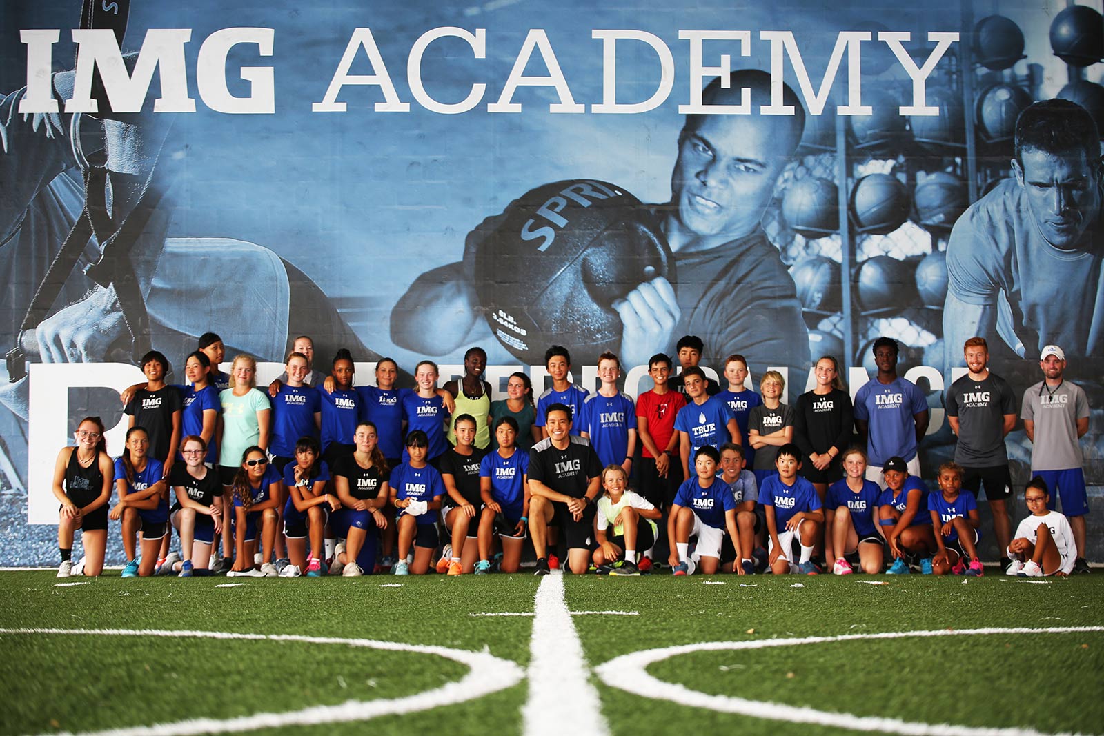 Yutaka taking a photo with a large group of students inside the indoor training turf