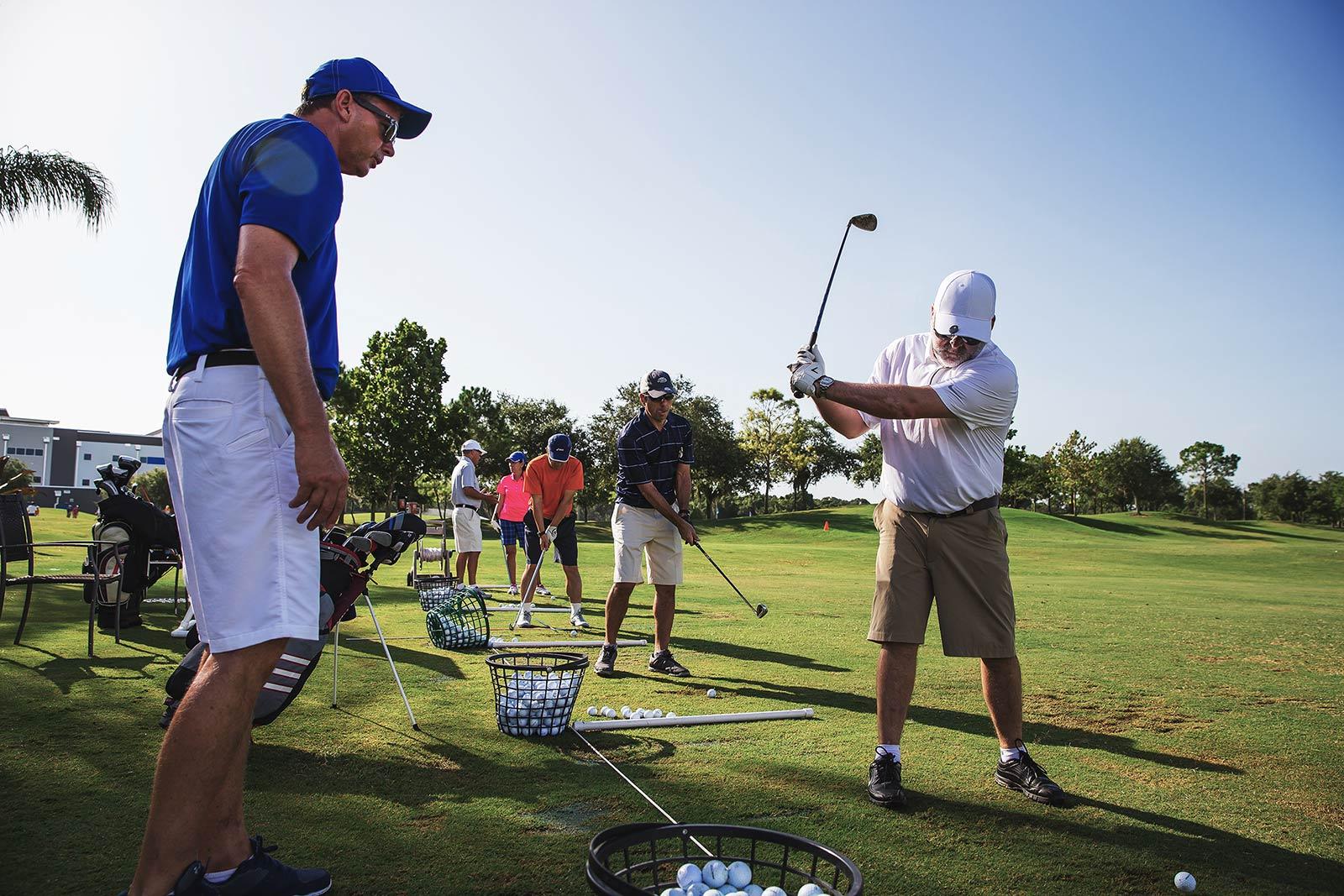 Golf coach assists adult golf camper with swing technique