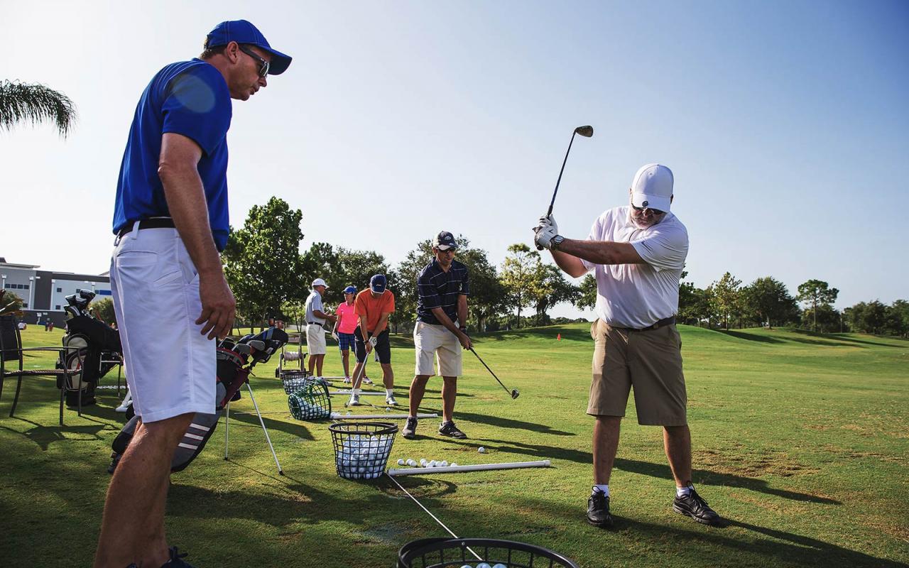 Golf coach assists adult golf camper with swing technique