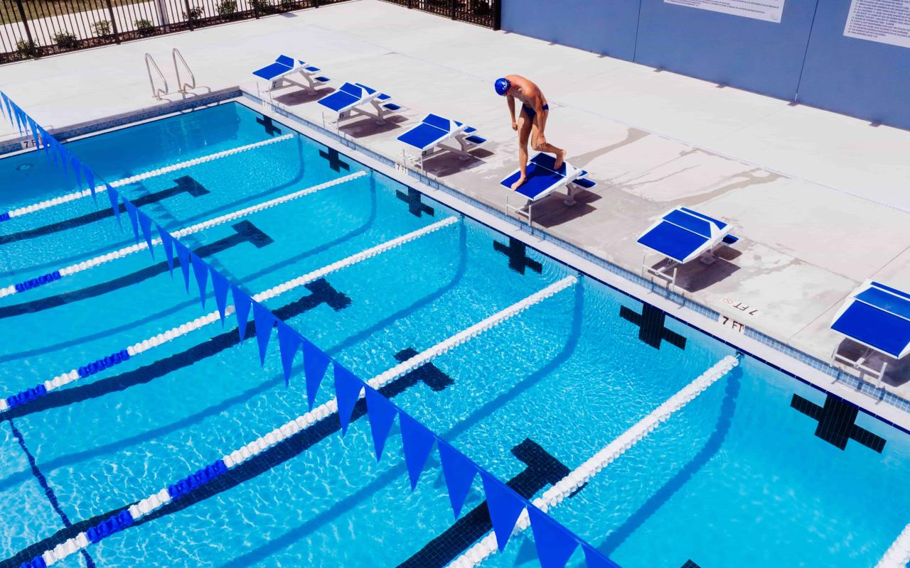 Wide angle shot of a swimmer on the starting block on the edge of an outdoor competition pool