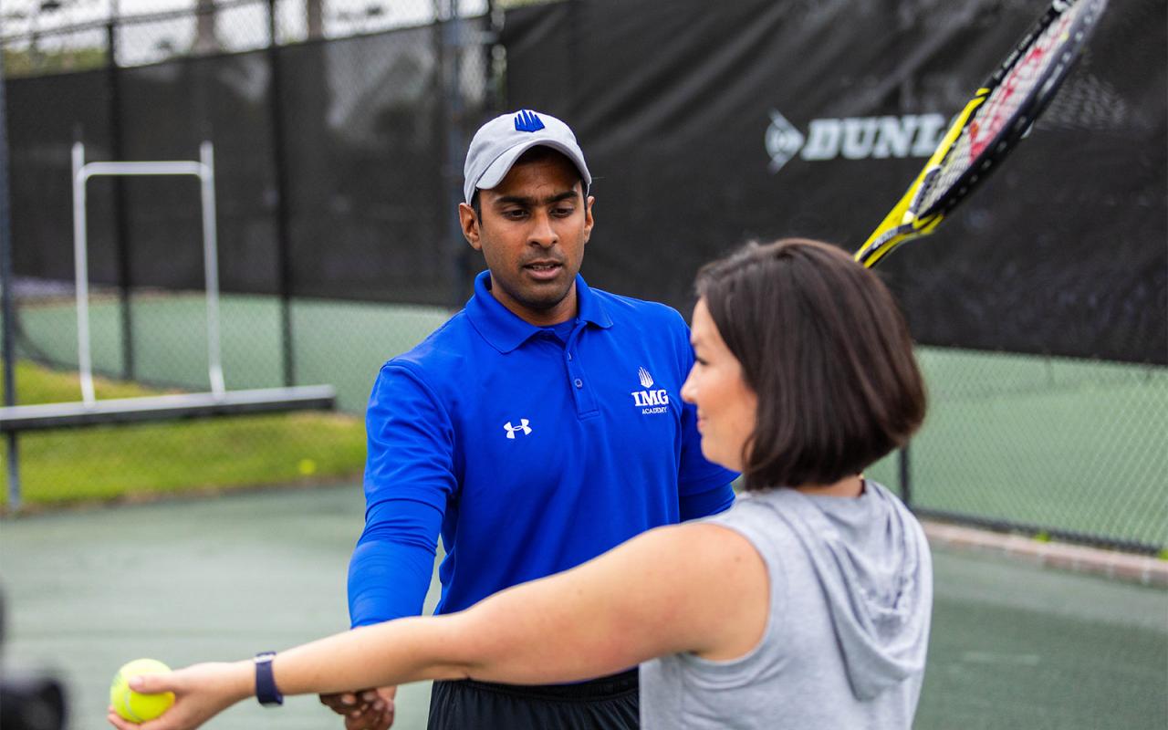 Tennis coach assisting adult tennis camper with tennis technique